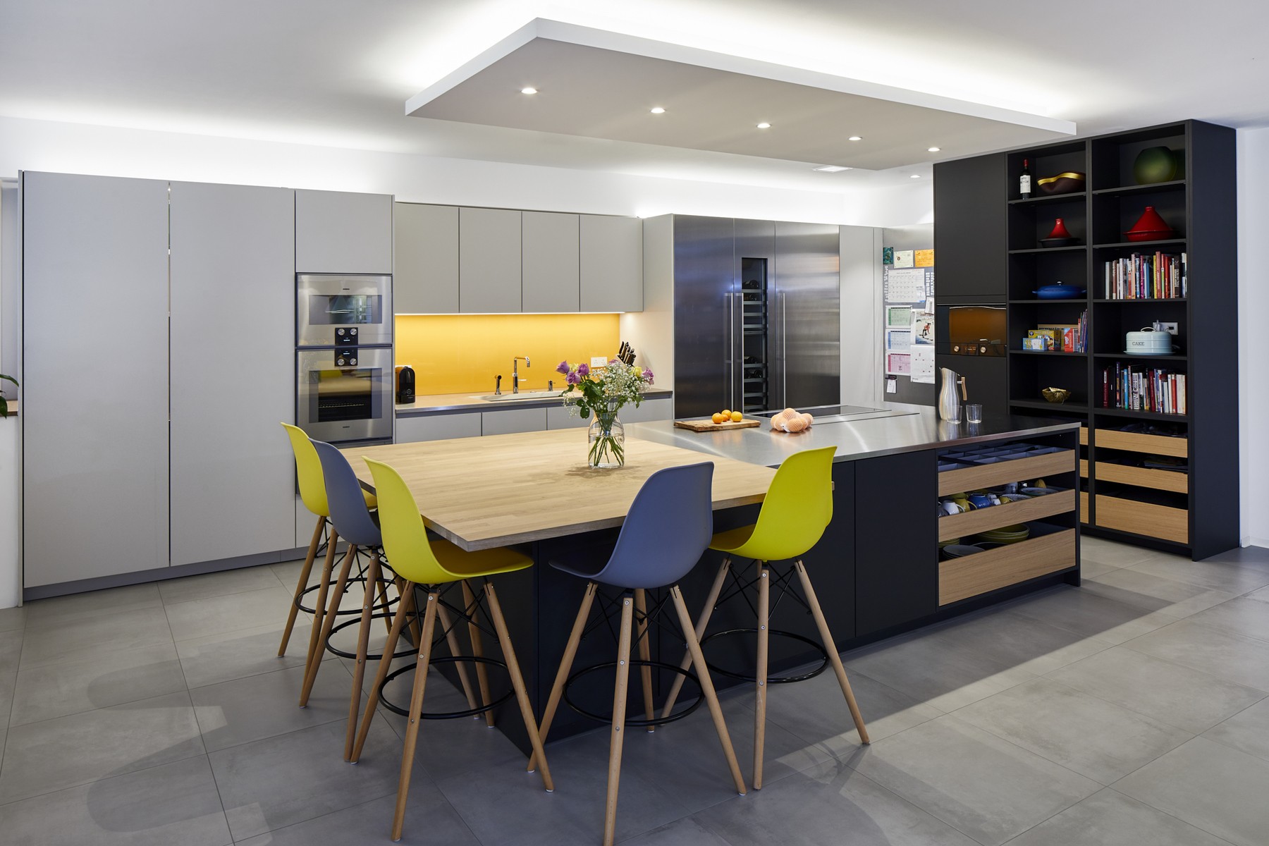 Modern kitchen with large island, colourful chairs, sleek cabinetry, and warm yellow/orange backsplash