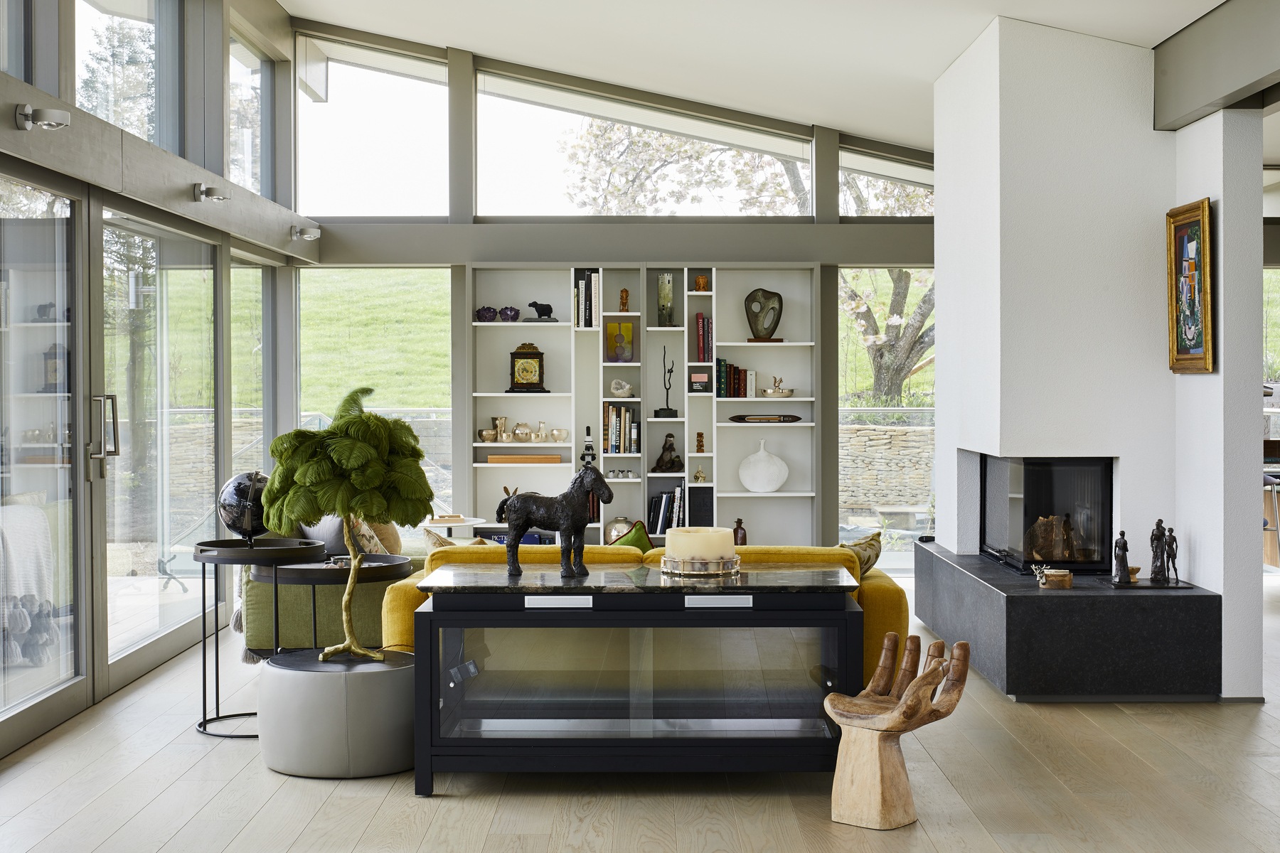 Modern living room with glass walls, open shelving, a fireplace, and eclectic decor.