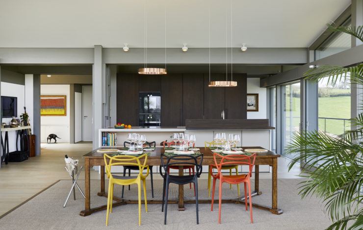 Modern dining area with colourful chairs, wooden table, open kitchen, and floor-to-ceiling windows