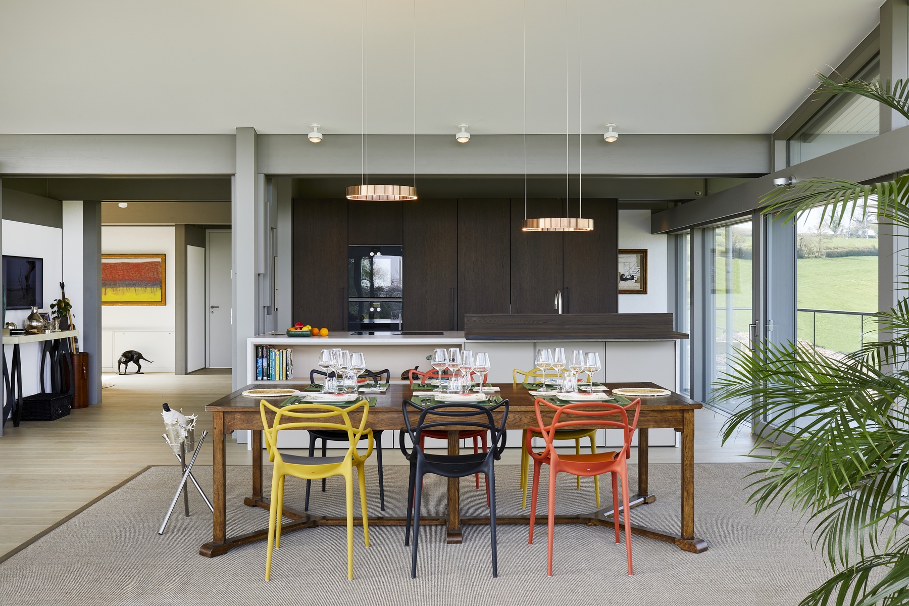 Modern dining area with colourful chairs, wooden table, open kitchen, and floor-to-ceiling windows