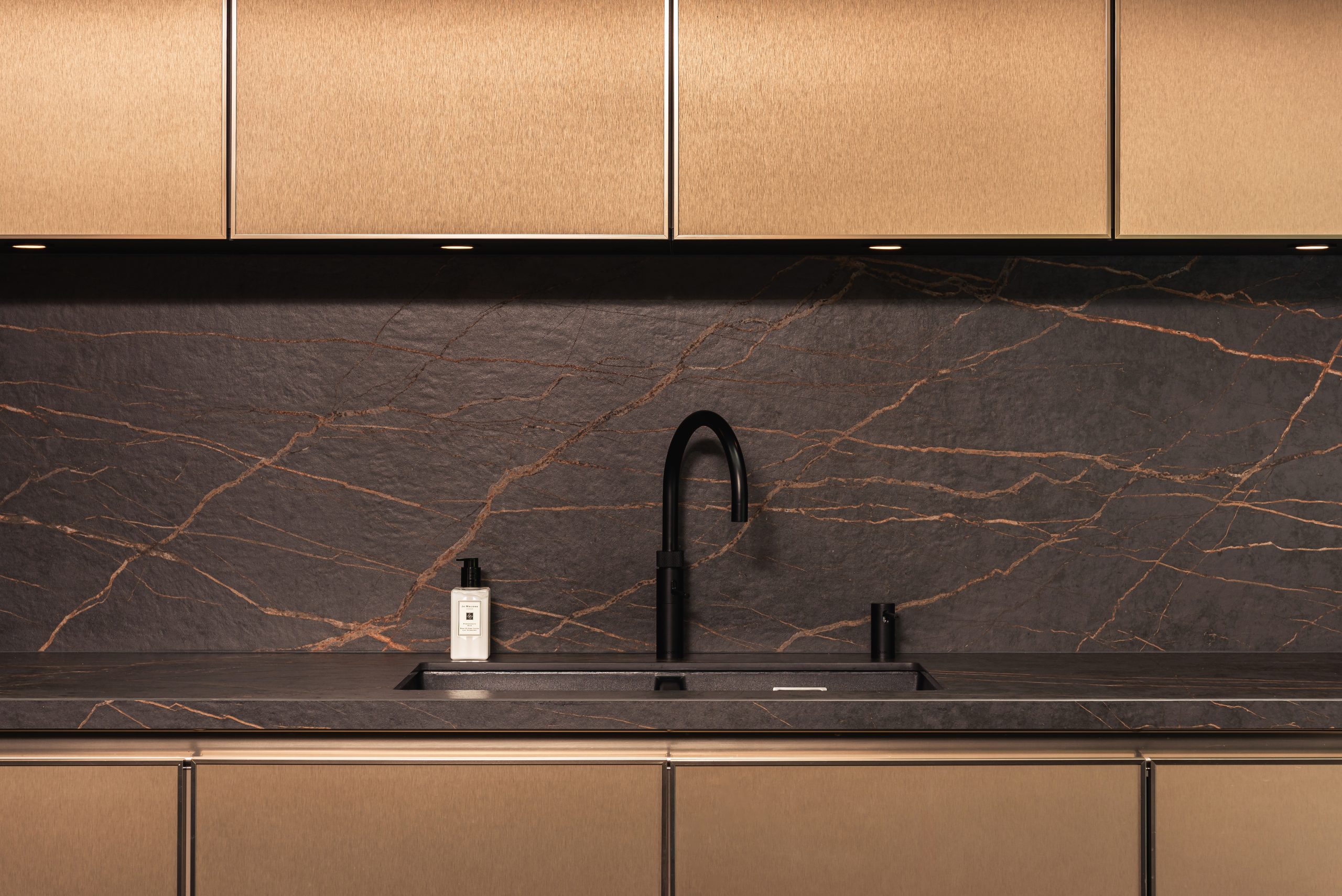 Close-up of a modern kitchen with black faucet, dark marble backsplash, and bronzed cabinetry