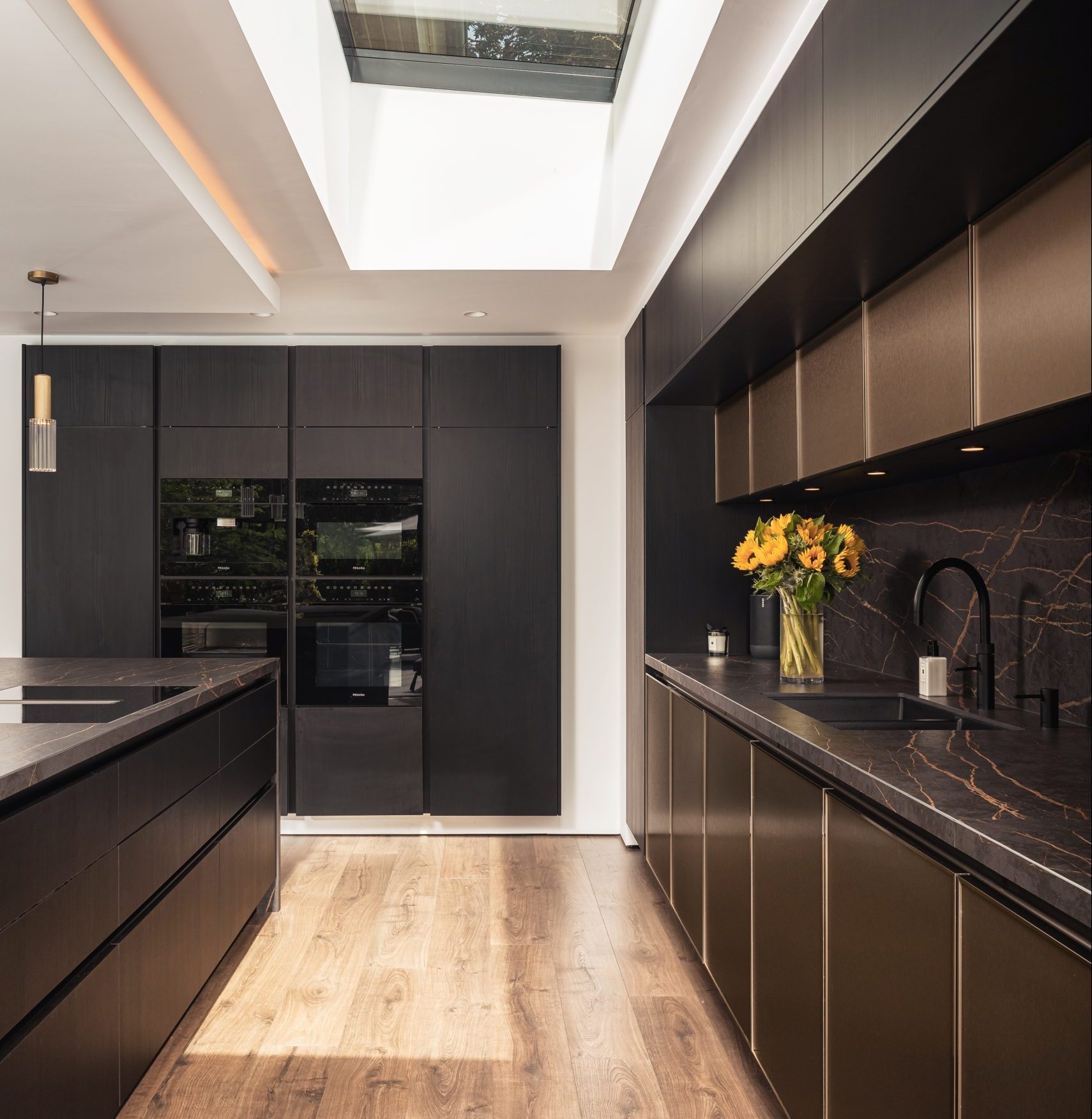 Modern kitchen with dark cabinetry, marble countertops, skylight, and sunflowers on the counter