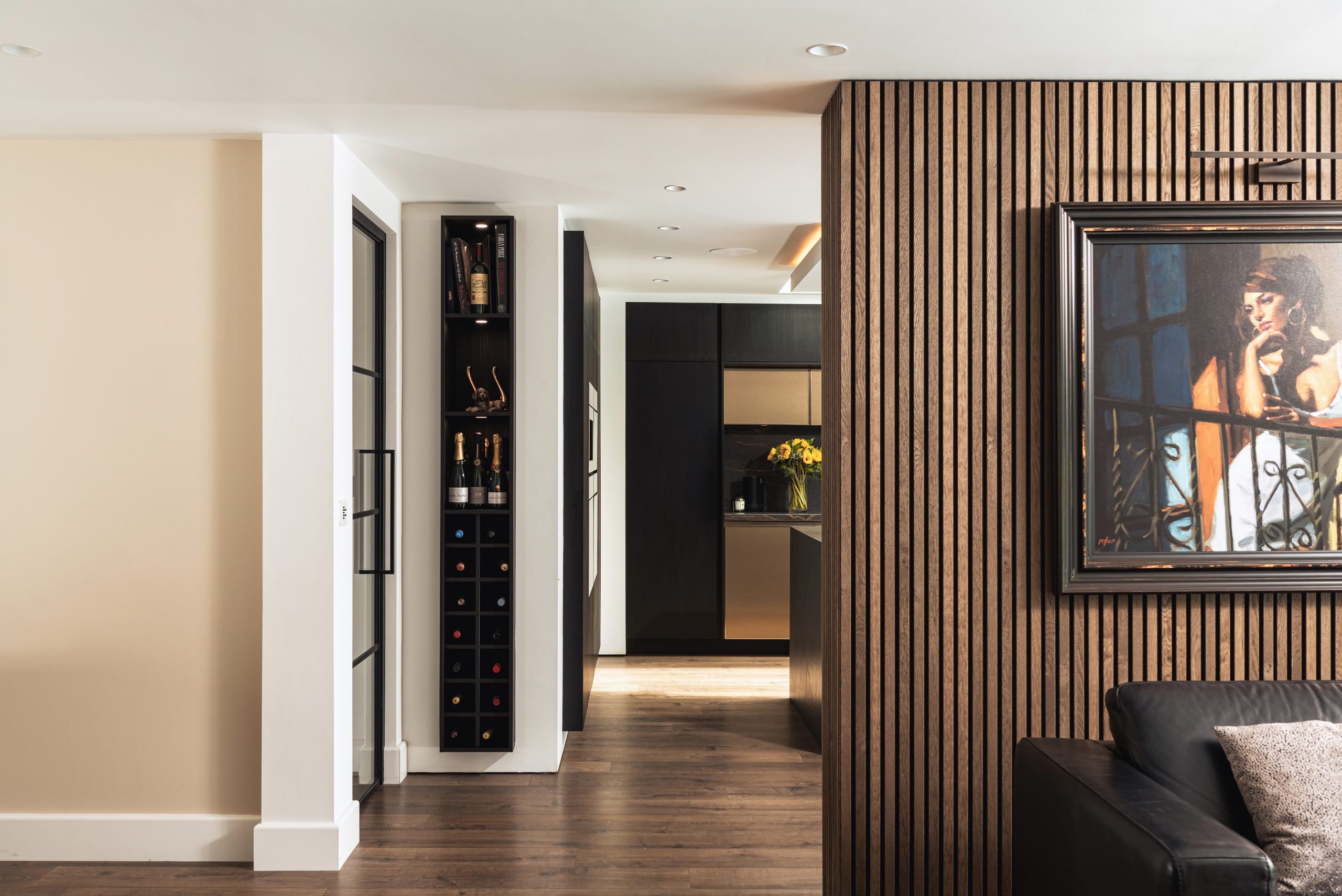 Hallway view into modern kitchen with wine rack, wood panelling, and framed painting on the wall