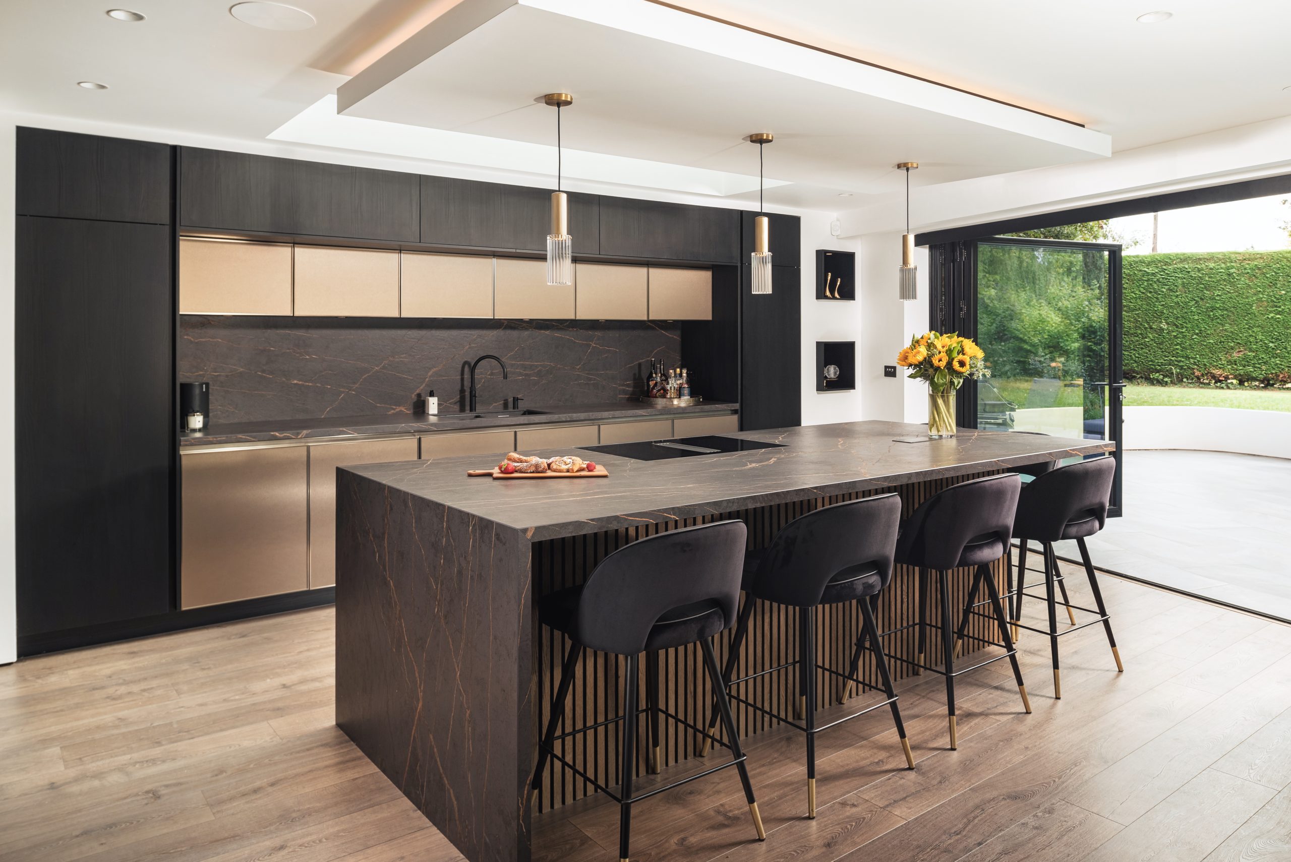 Sleek modern kitchen with large island, dark cabinetry, gold accents, and floor-to-ceiling windows