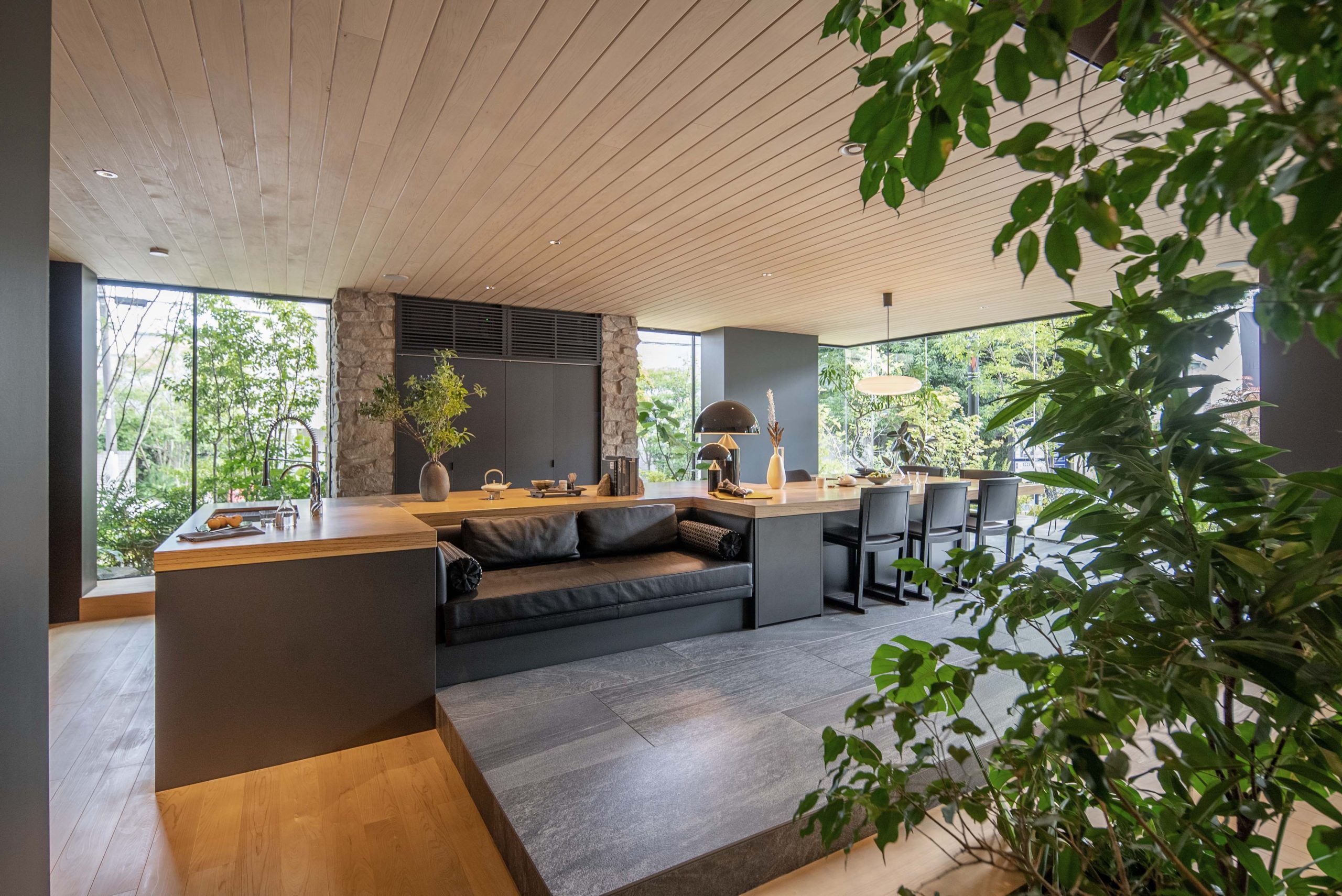 Modern open-plan, Japanese style kitchen with wood and stone accents, built-in seating, and floor-to-ceiling windows and plants