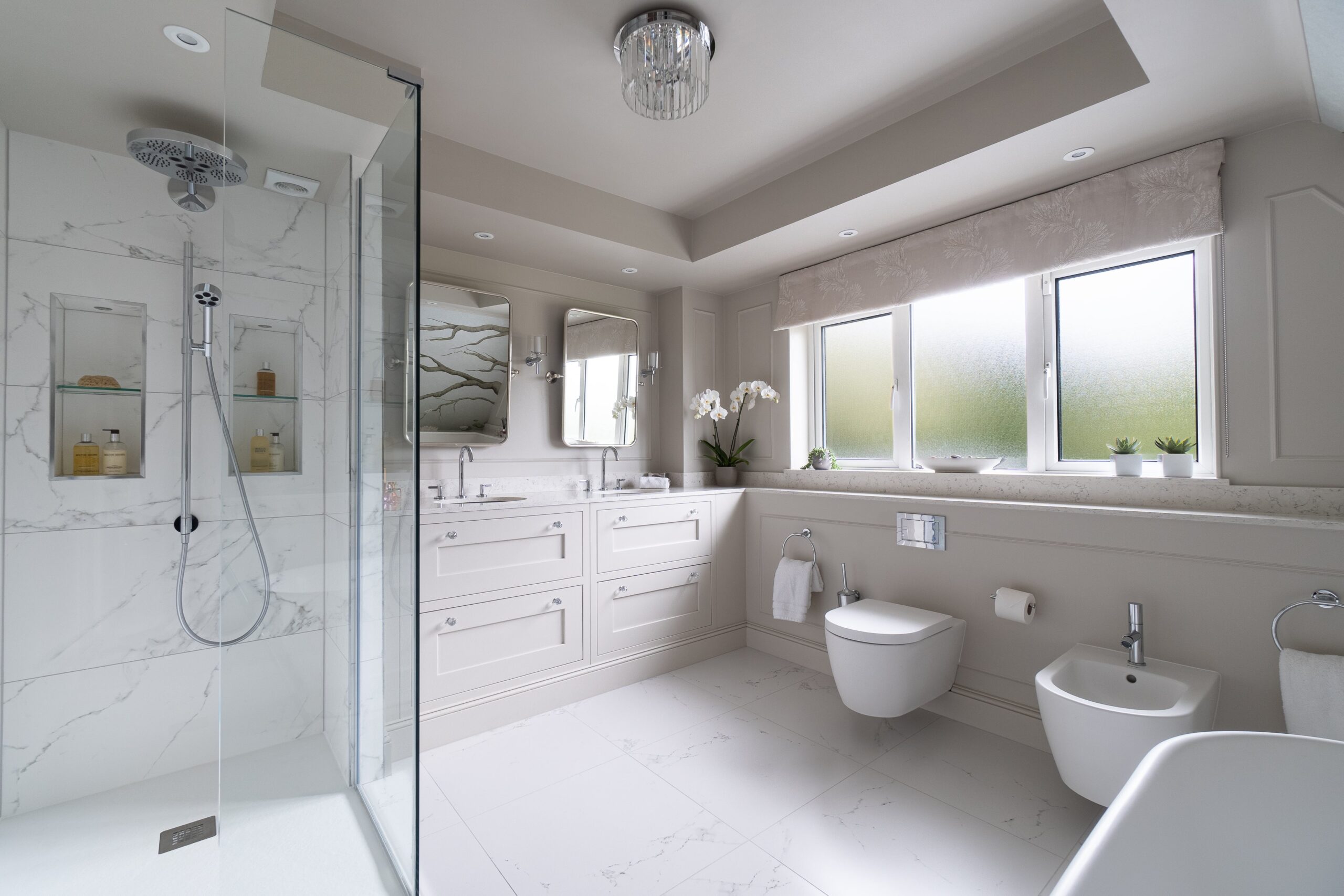 Modern bathroom with marble tiles, glass shower, double vanity, wall-hung toilet, and frosted window.