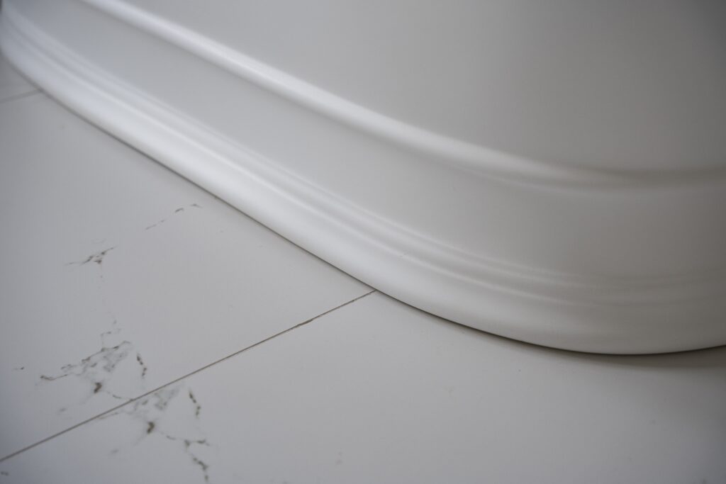 Close-up of a white bathtub base on marble floor tiles with subtle veining