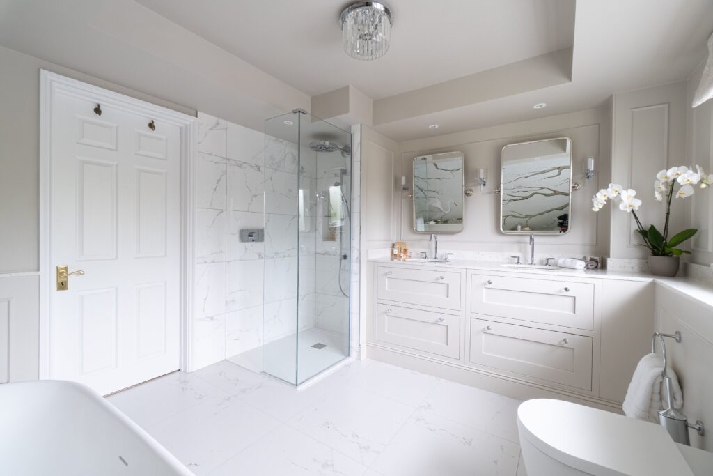 Bright bathroom with marble shower, double vanity, mirrors, and orchid on countertop.