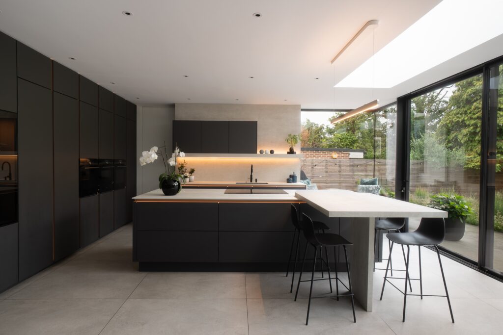 Modern kitchen with dark cabinets, island, bar stools, and large windows overlooking a garden